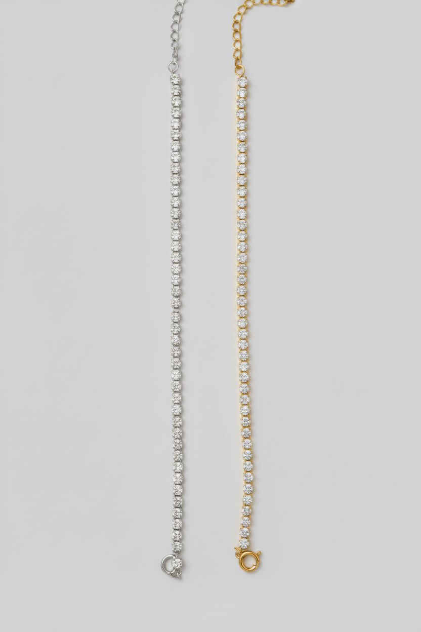 Two delicate chain bracelets displayed vertically side-by-side on a neutral gray background. One bracelet is silver-toned with clear stones, and the other is gold-toned with clear stones.