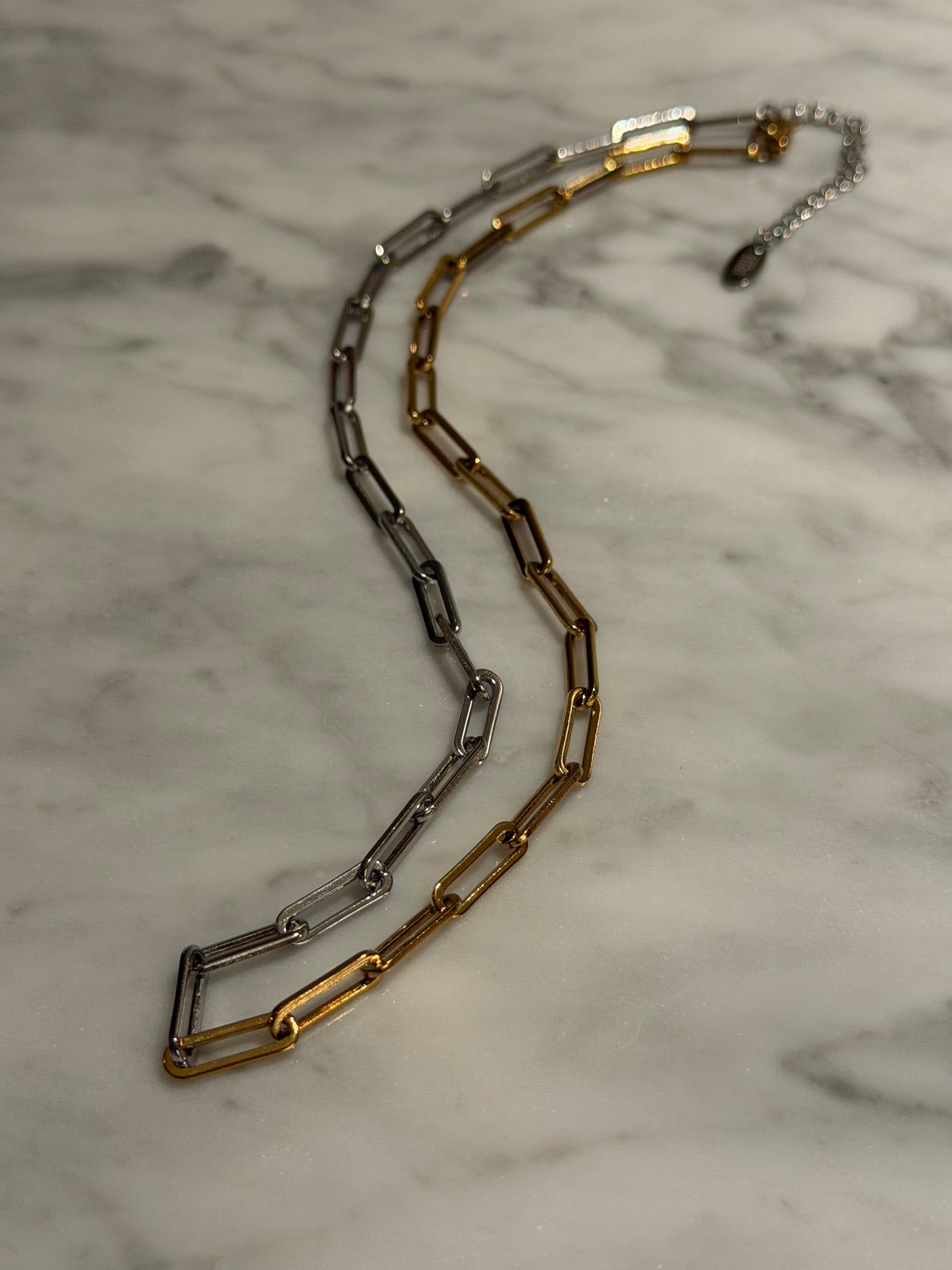Two gold and silver chain necklace on a marble surface
