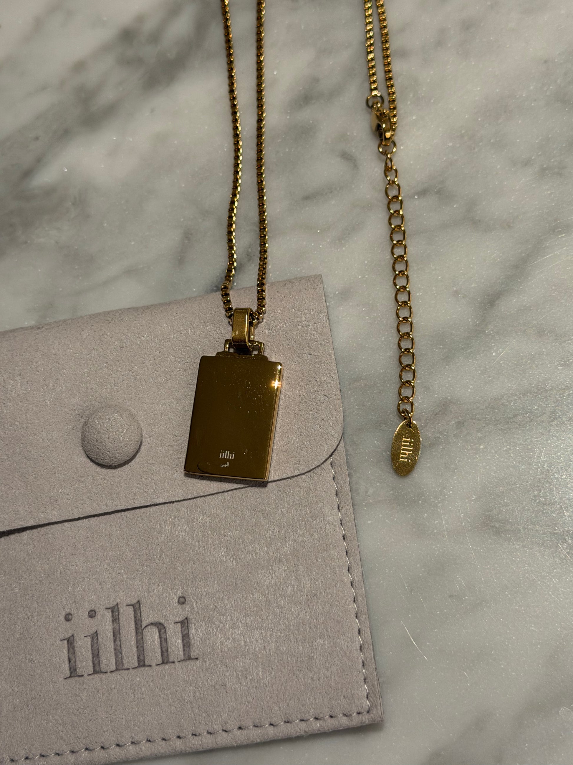 Gold necklace with pendant on a gray surface next to a gray card with 'iilhi' branding.