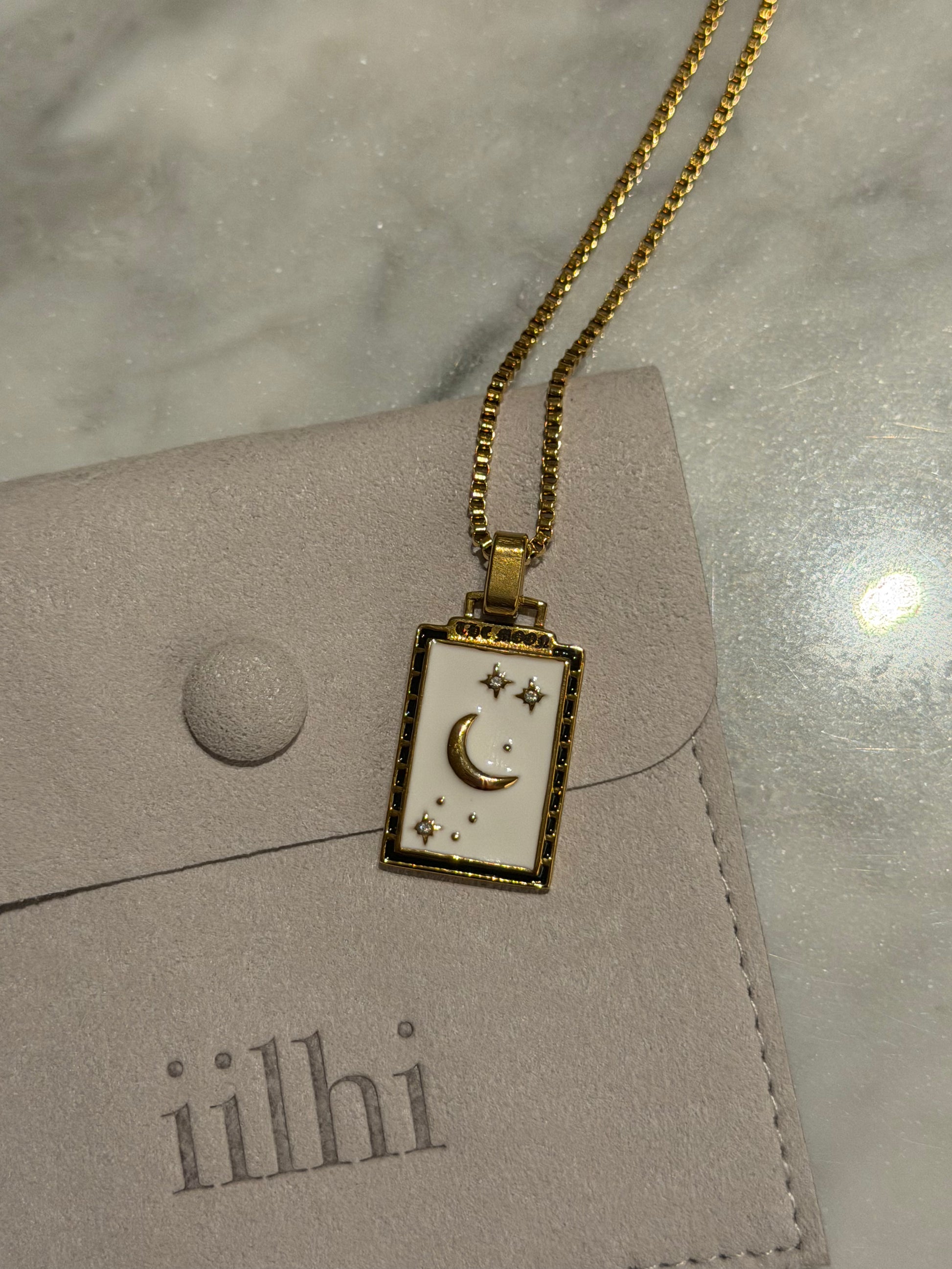 Gold necklace with a moon and star pendant on a gray surface with 'iilhi' branding.