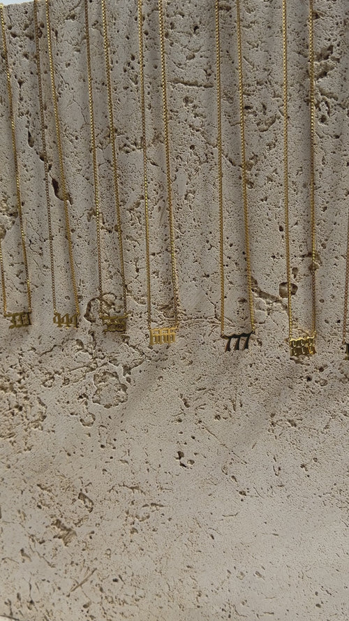 Gold angel number necklaces on travertine background